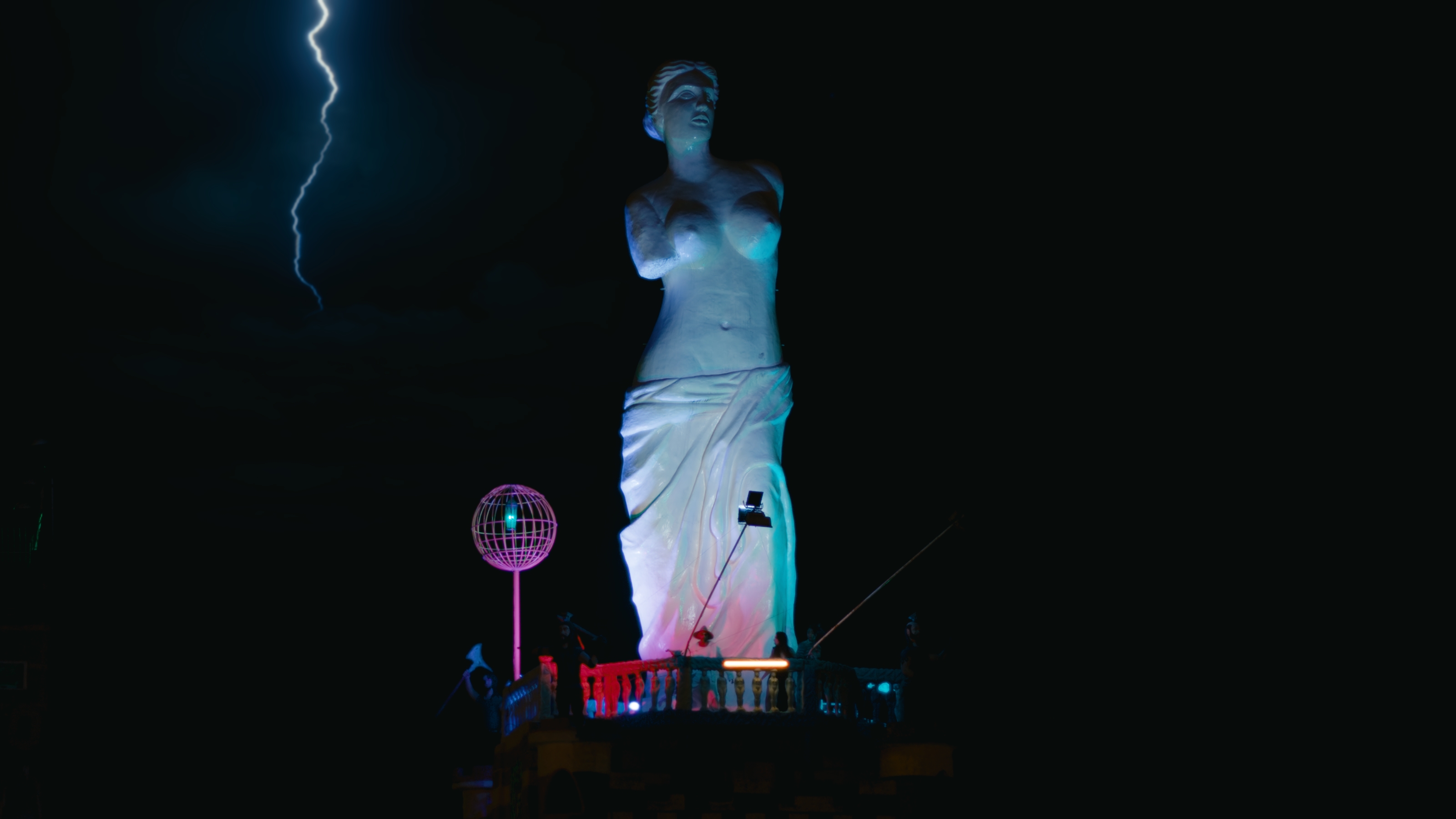 A towering Venus statue illuminated in blue and pink beneath lightning at the My Little Pony motel
