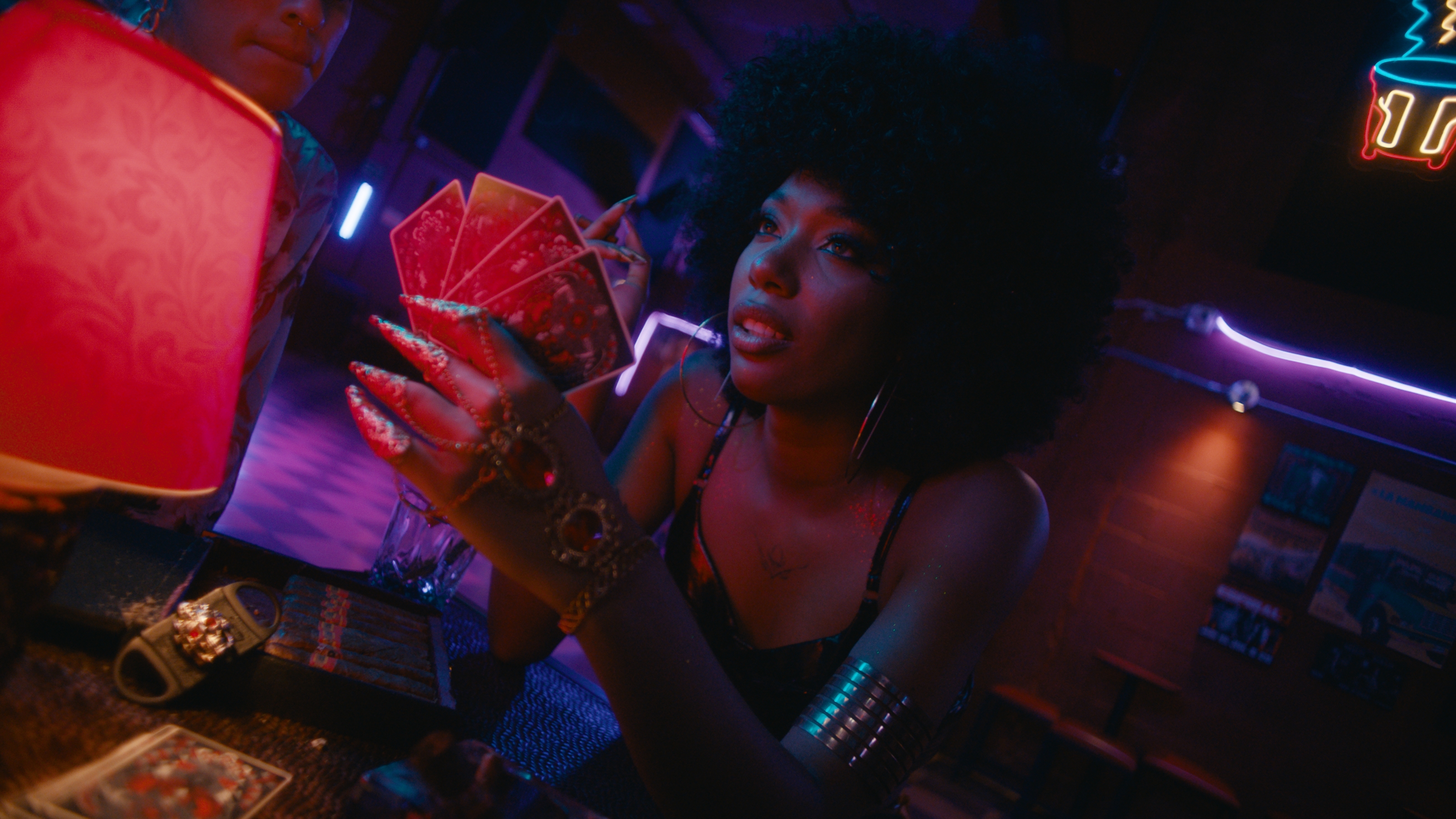 La Flaca holding her cards in the neon-lit bar