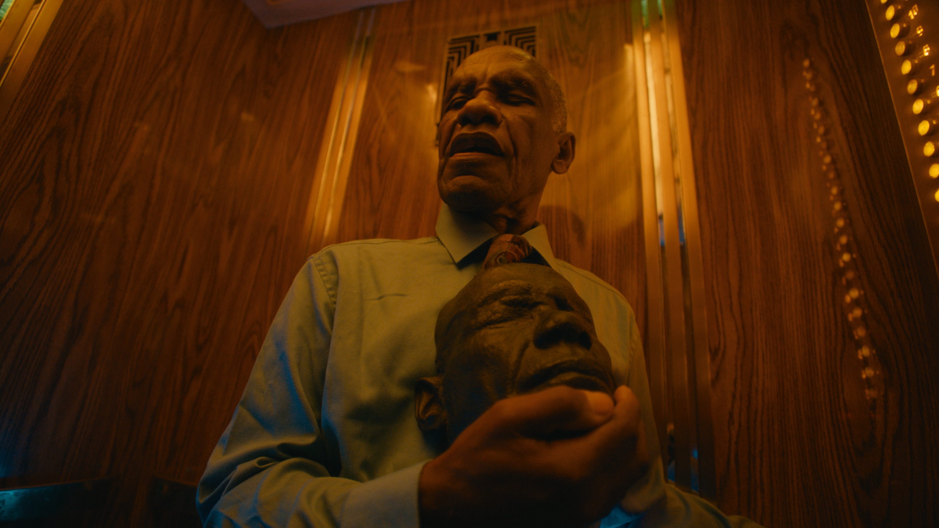 A man holding a carved mask in a wood-paneled elevator